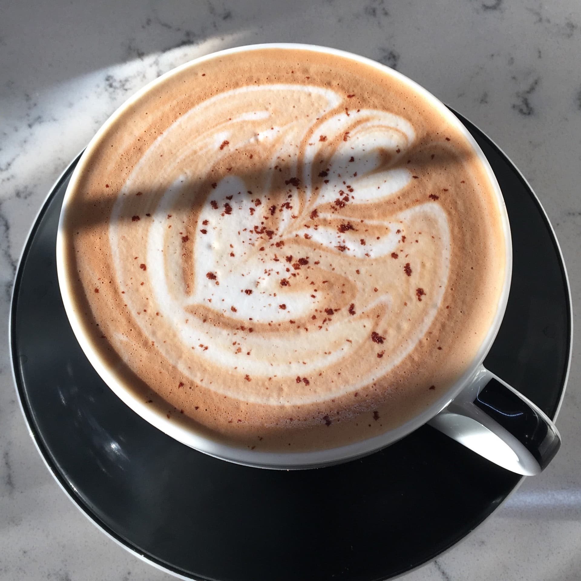 Latte with leaf art beside stacked assorted donuts on dark table against exposed brick wall 4