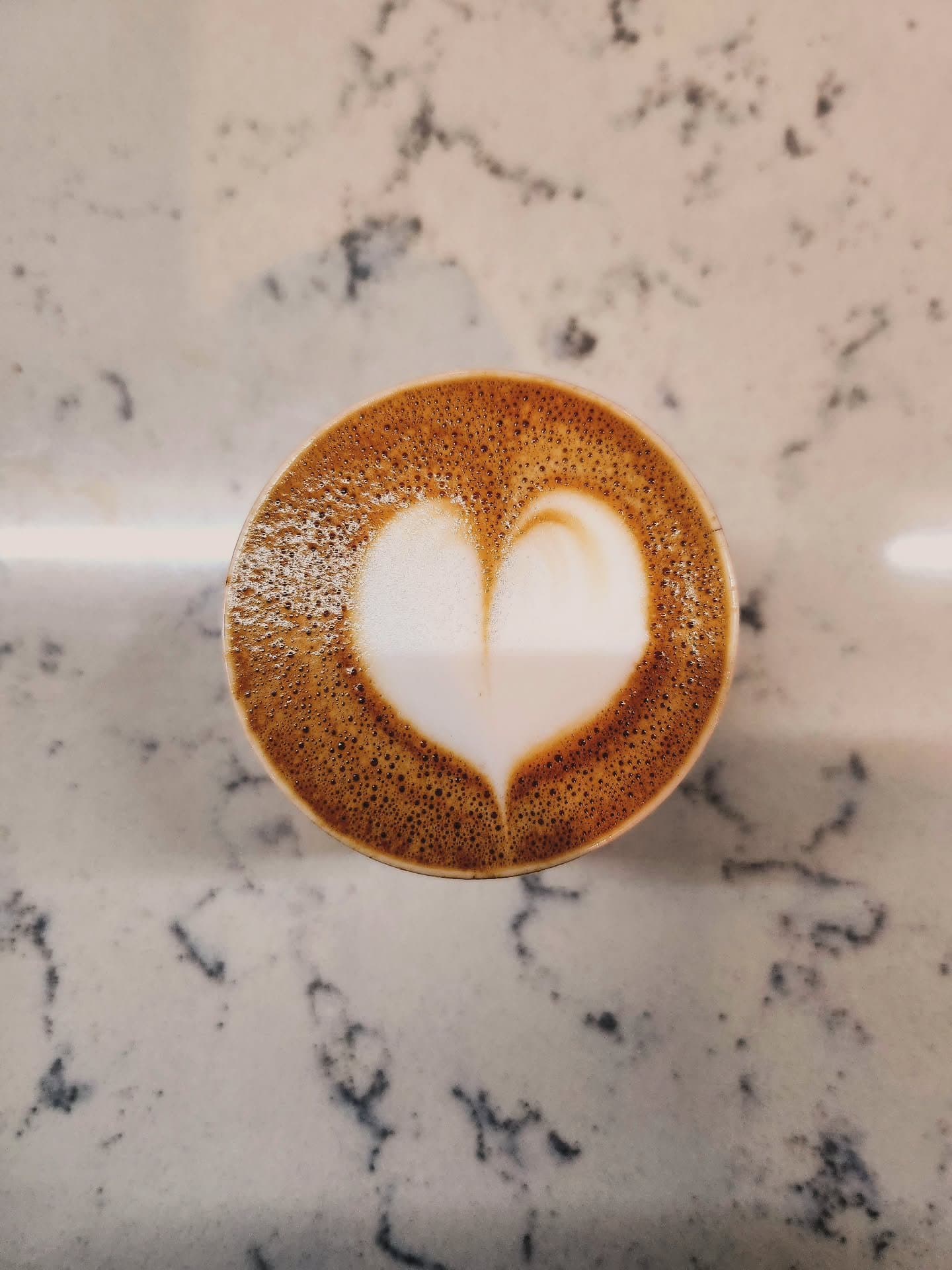 Latte with leaf art beside stacked assorted donuts on dark table against exposed brick wall 6