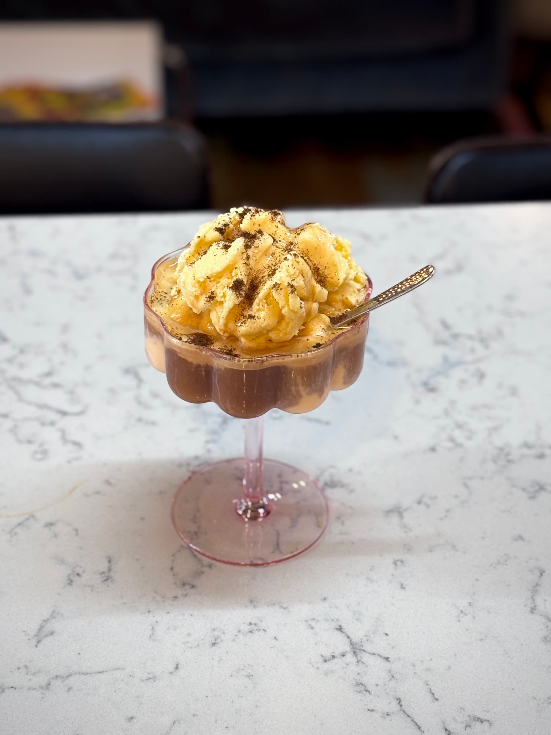Creamy vanilla ice cream with espresso in a pink coupe glass, topped with cocoa powder and a gold spoon 1